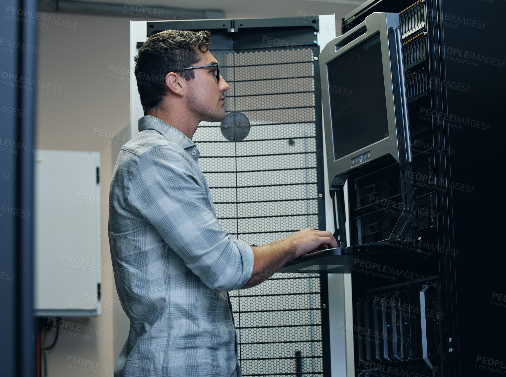 Buy stock photo Cropped shot of a handsome young male programmer working on a computer in a server room