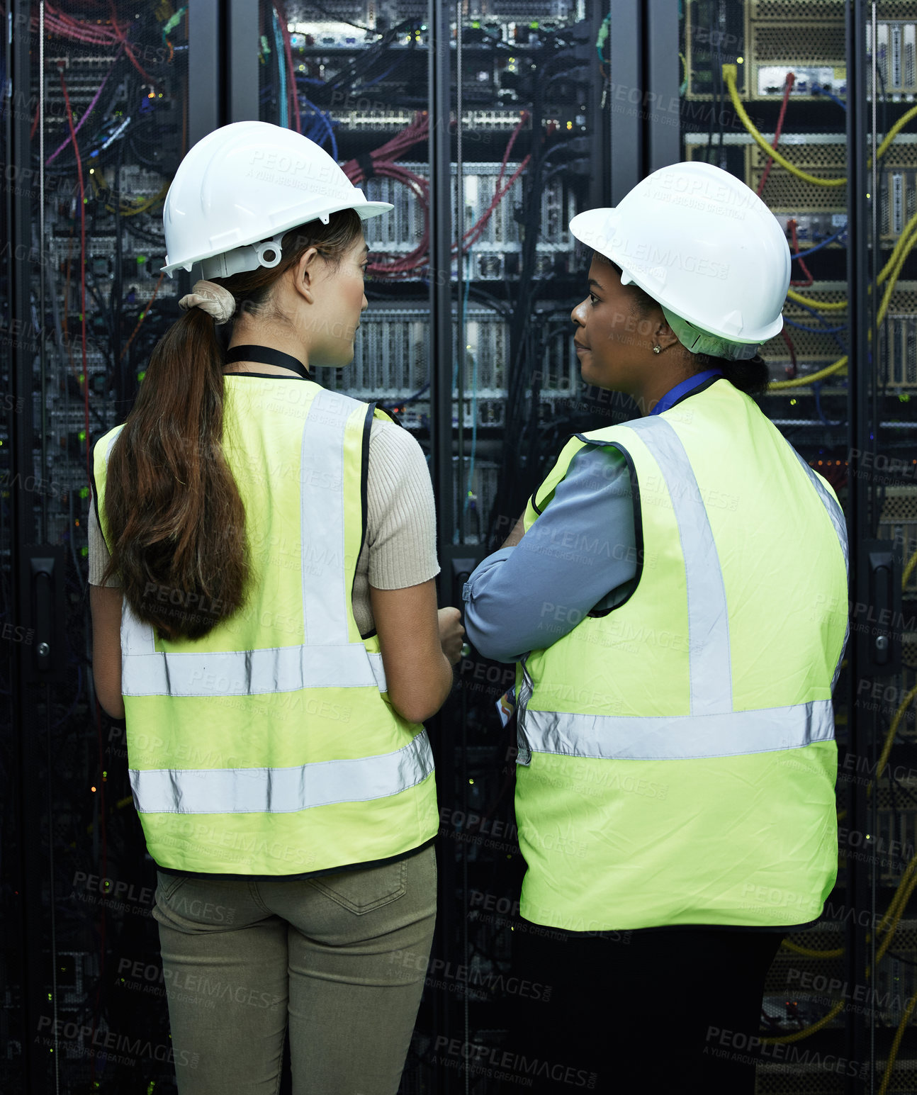 Buy stock photo Rearview shot of two attractive female programmers working in a server room