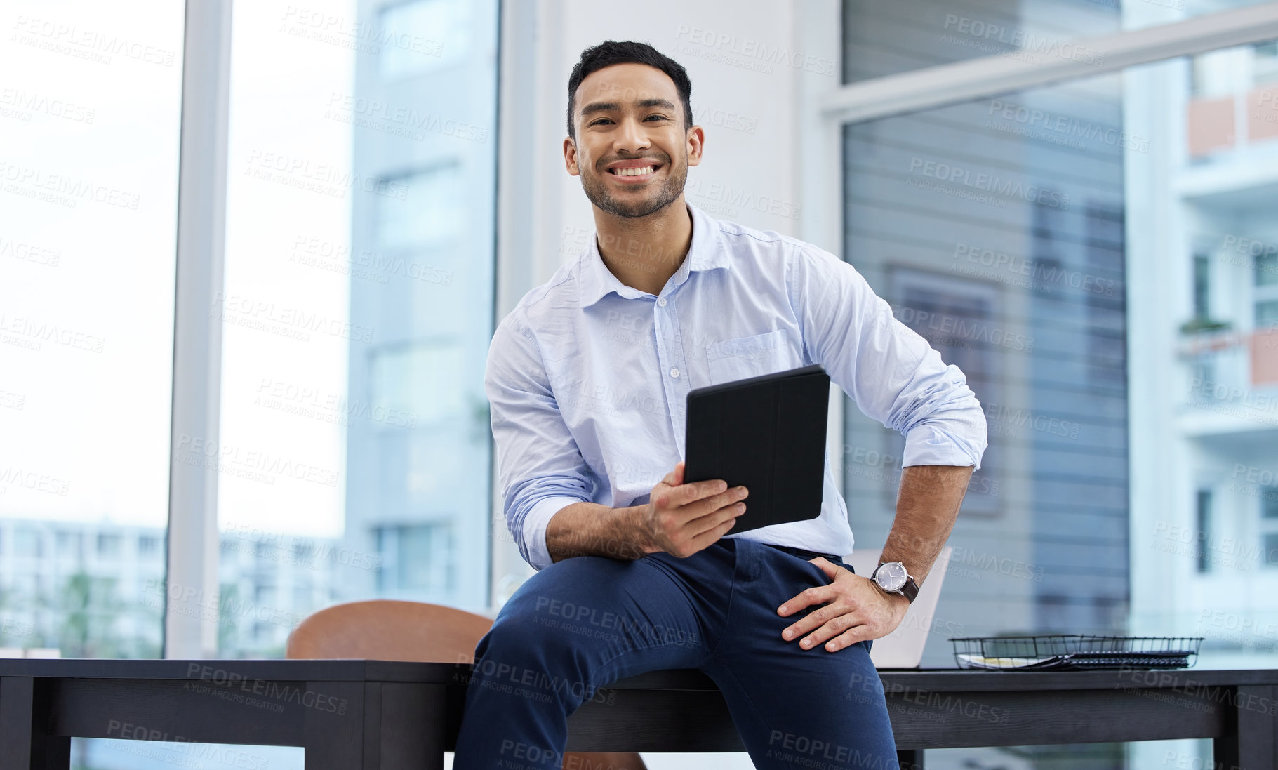 Buy stock photo Shot of a handsome young businessman sitting alone in his office and holding a digital tablet