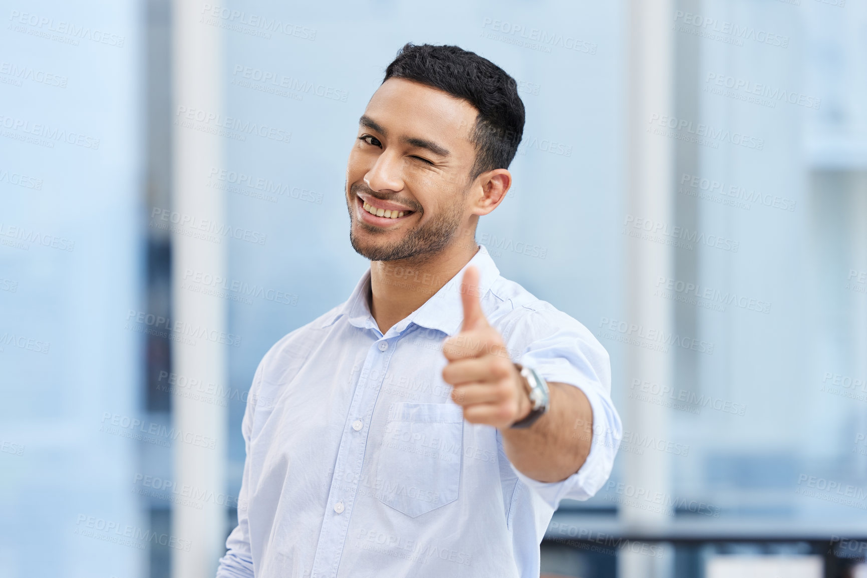 Buy stock photo Shot of a handsome young businessman standing alone in the office and making a thumbs up gesture