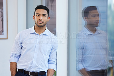 Buy stock photo Shot of a handsome young businessman standing alone in the office during the day