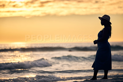 Buy stock photo Shot of an unrecognizable woman walking along the beach at sunset