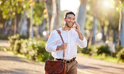 Buy stock photo Shot of a handsome young businessman walking alone through the city and using his cellphone