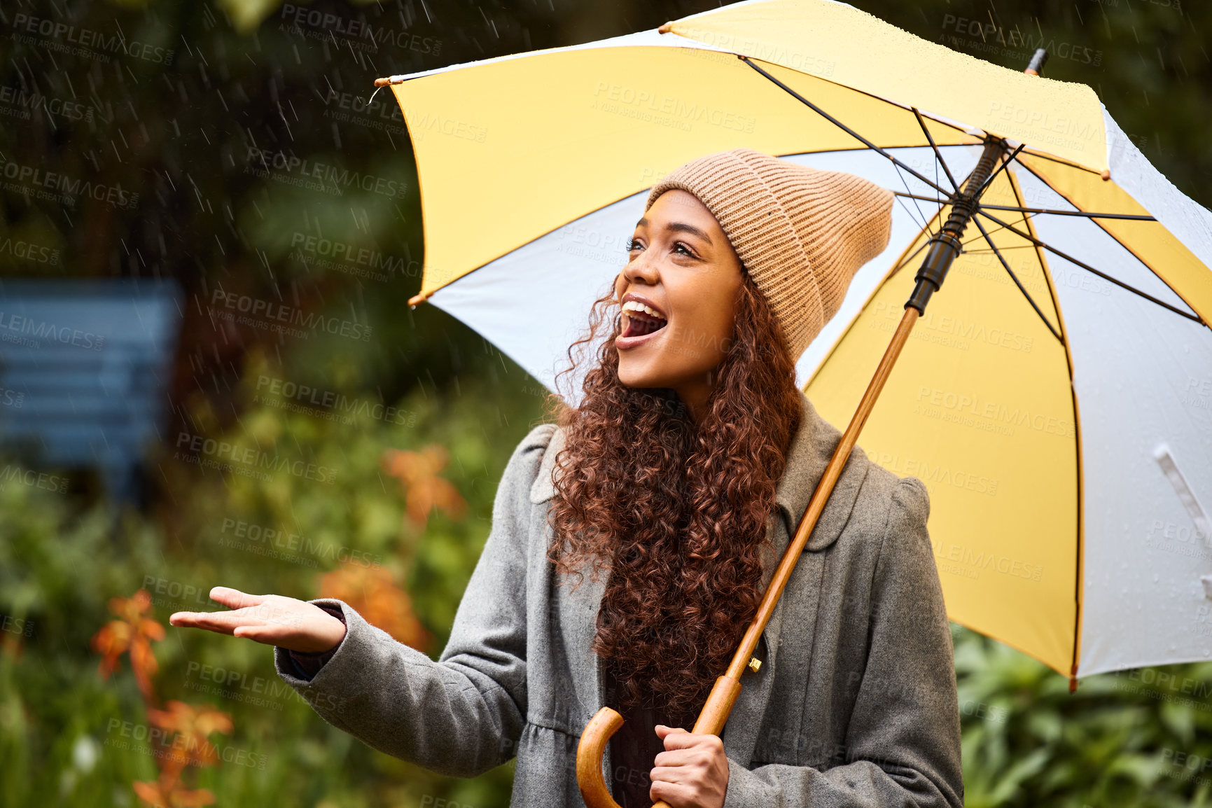 Buy stock photo Shot of a young woman standing in the rain with an umbrella