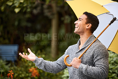 Buy stock photo Shot of a young man standing in the rain with an umbrella