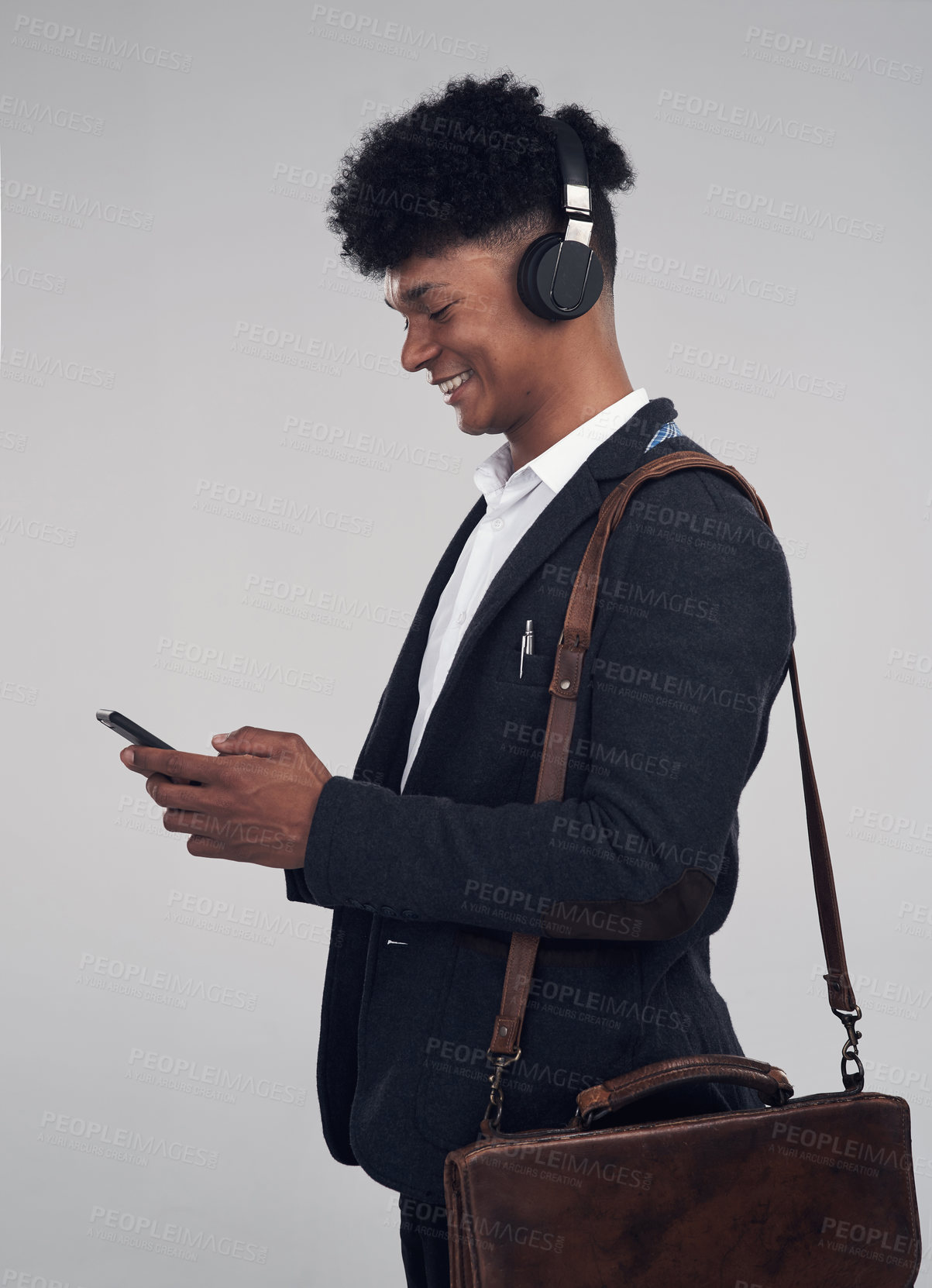 Buy stock photo Studio shot of a young businessman using a smartphone and headphones against a grey background