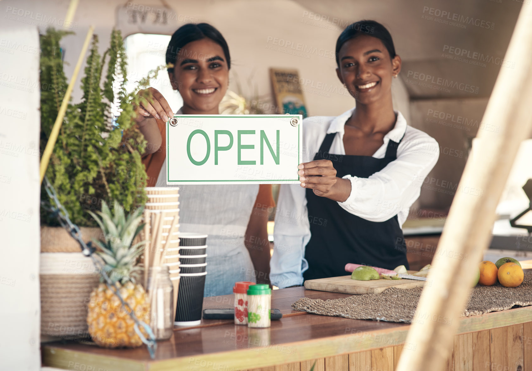 Buy stock photo Shot of two young businesswomen holding an open sign in their food truck