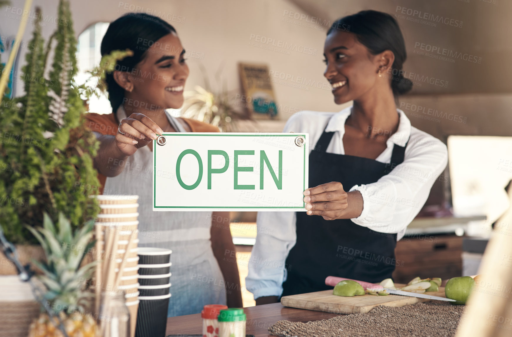 Buy stock photo Shot of two young businesswomen holding an open sign in their food truck