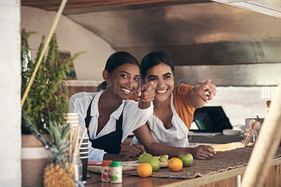 Buy stock photo Shot of two young businesswomen pointing from their food truck