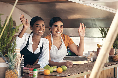 Buy stock photo Shot of two young businesswomen waving from their food truck