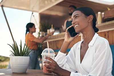 Buy stock photo Shot of a young woman drinking a smoothie while using her smartphone