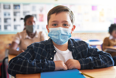 Buy stock photo Shot of a young boy sitting in his classroom at school and wearing a face mask