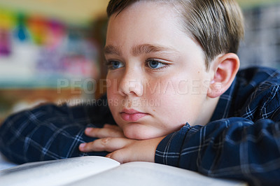 Buy stock photo Shot of a young boy sitting alone in his classroom at school and feeling bored