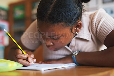 Buy stock photo Shot of a young girl sitting alone in her classroom at school and writing in her workbook