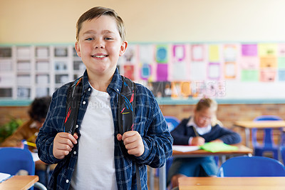 Buy stock photo Shot of a young boy standing in his classroom at school and holding his backpack
