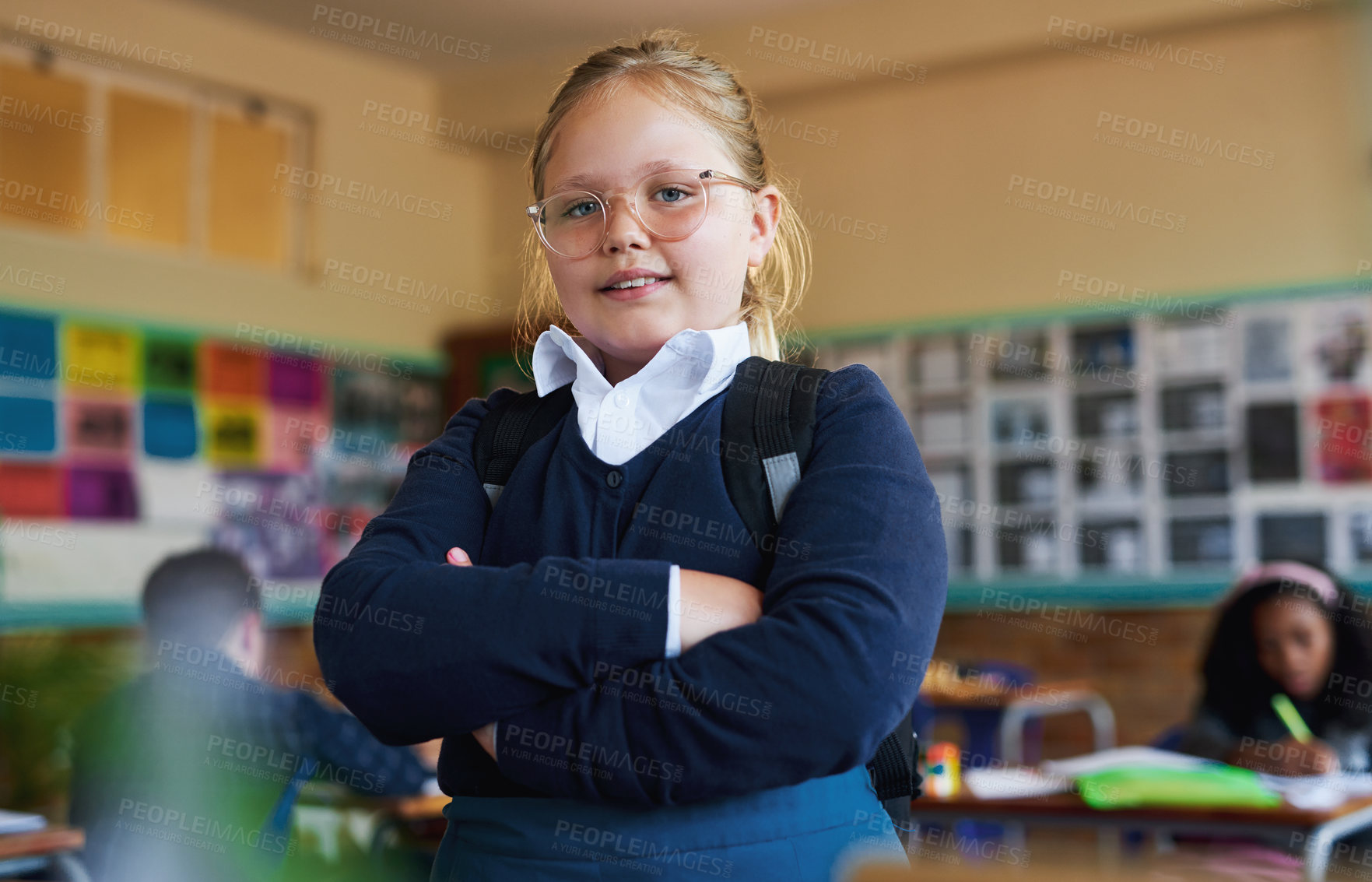 Buy stock photo Shot of a young girl standing in her classroom at school with her arms folded