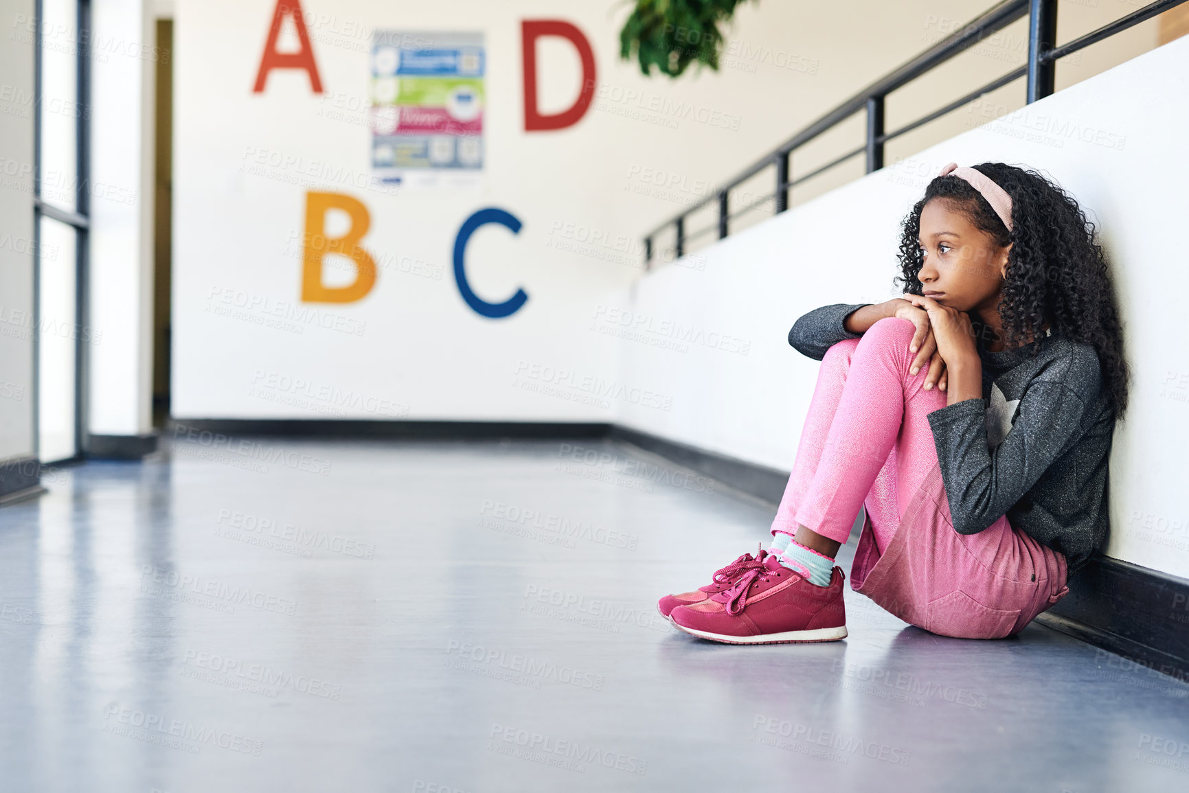 Buy stock photo Full length shot of a young girl sitting alone in the hallway at school and feeling depressed