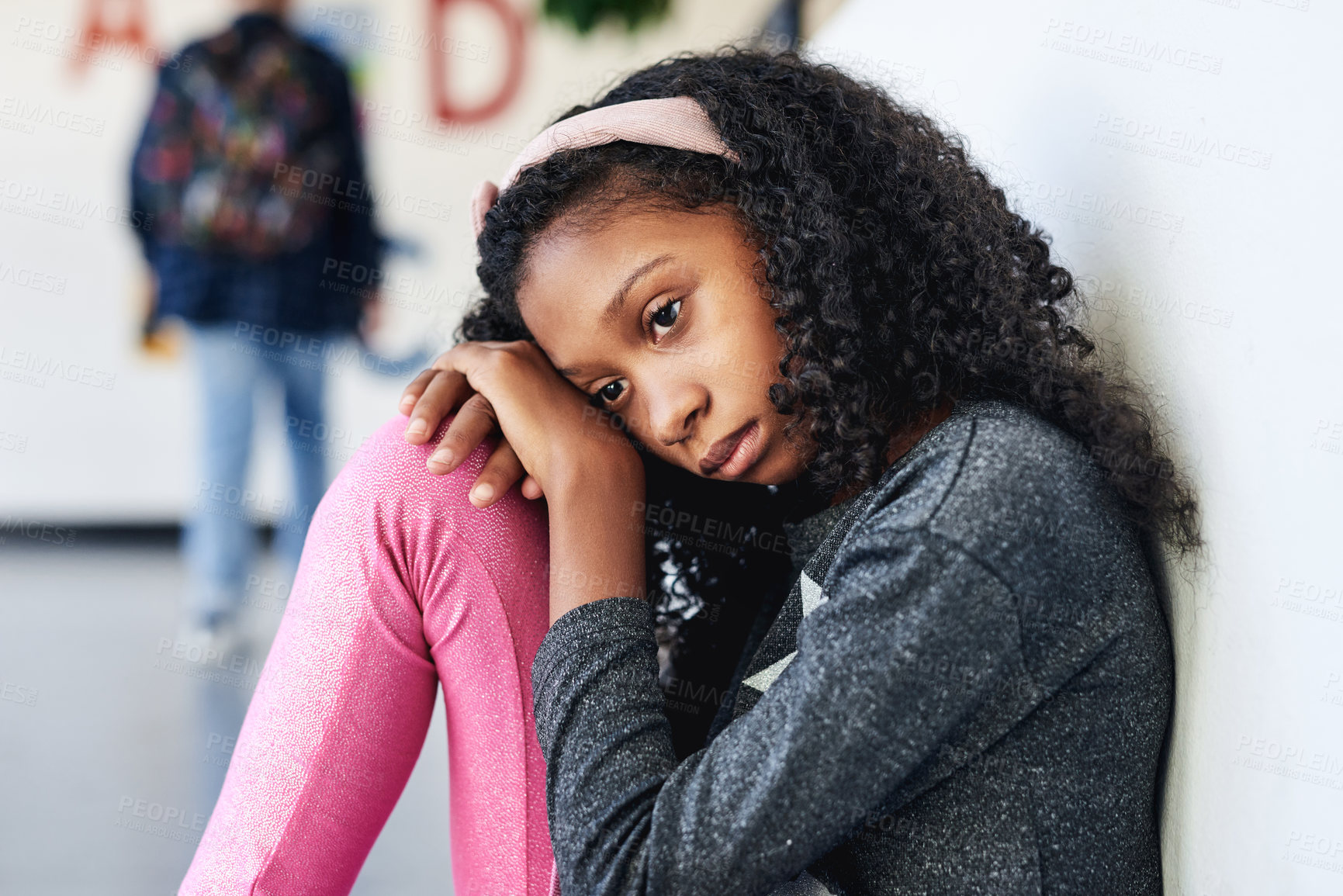 Buy stock photo Shot of a young girl sitting in the hallway at school and feeling depressed