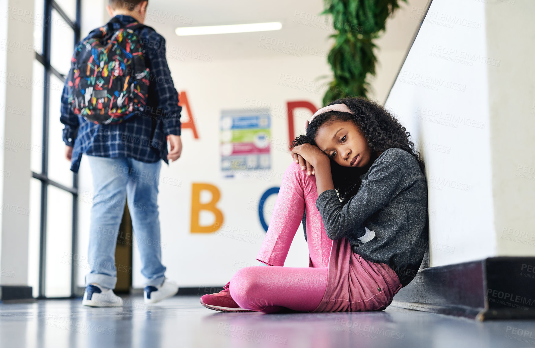 Buy stock photo Full length shot of a young girl sitting in the hallway at school and feeling depressed