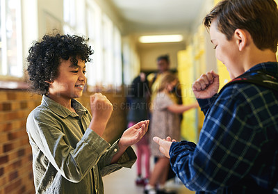 Buy stock photo Shot of two young boys standing in the school hallway together and playing a game of rock, paper and scissors