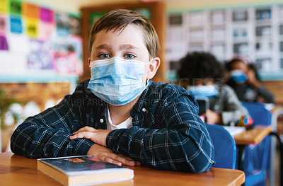 Buy stock photo Shot of a young boy sitting in his classroom at school and wearing a face mask