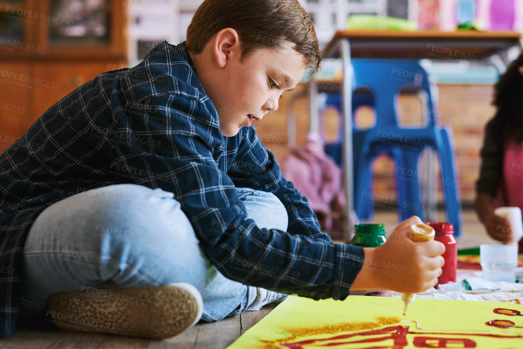 Buy stock photo Shot of a young boy sitting on the floor in his classroom during an art class