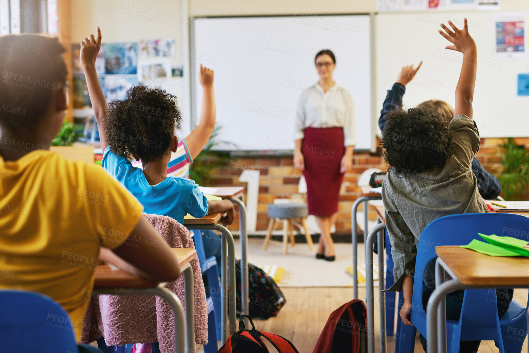 Buy stock photo Shot of an unrecognizable group of children sitting in their school classroom and raising their hands to answer a question