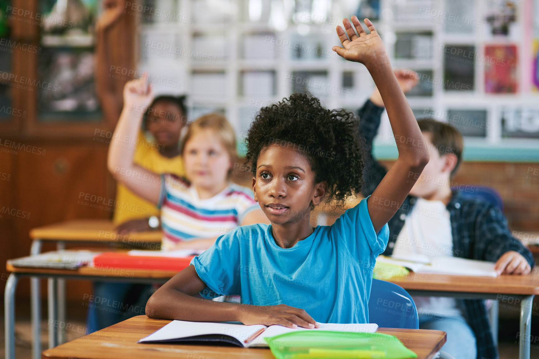 Buy stock photo Shot of a diverse group of children sitting in their school classroom and raising their hands to answer a question