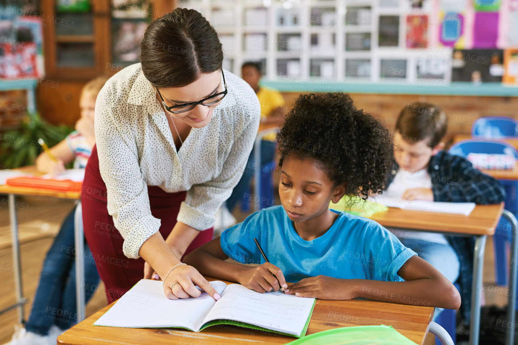 Buy stock photo Shot of an attractive young teacher helping a student in her classroom during a lesson