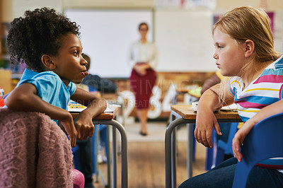 Buy stock photo Shot of a young girl sitting in the classroom at school and pulling her tongue out at her classmate