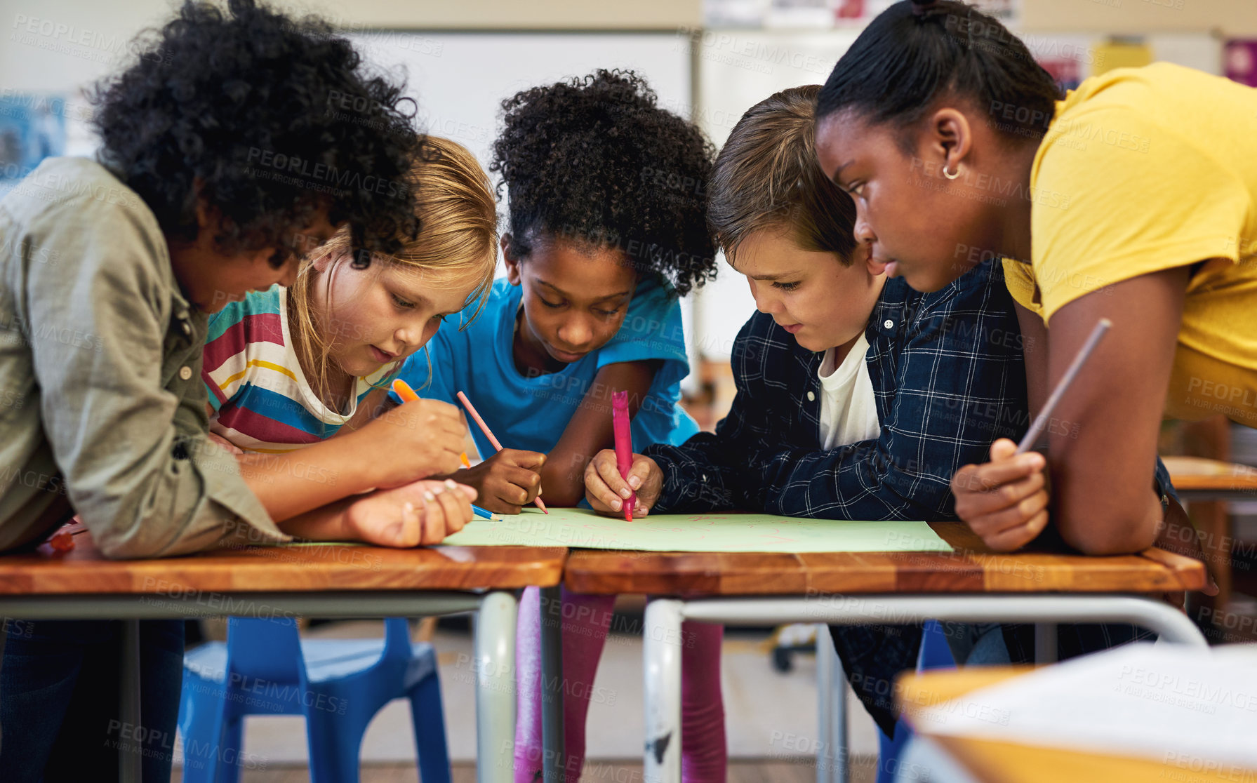 Buy stock photo Shot of a diverse group of children huddled together and colouring in their classroom at school