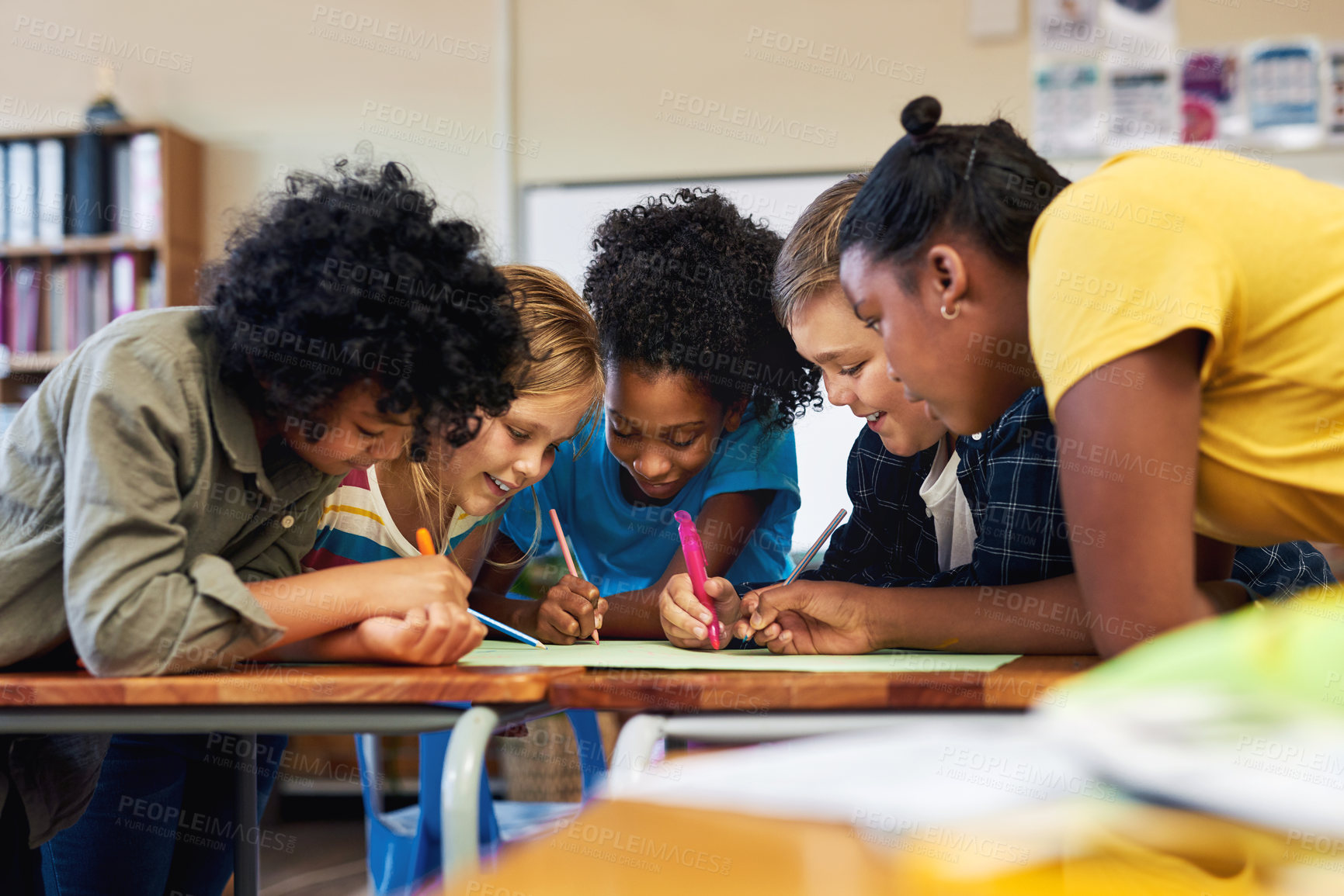 Buy stock photo Shot of a diverse group of children huddled together and colouring in their classroom at school