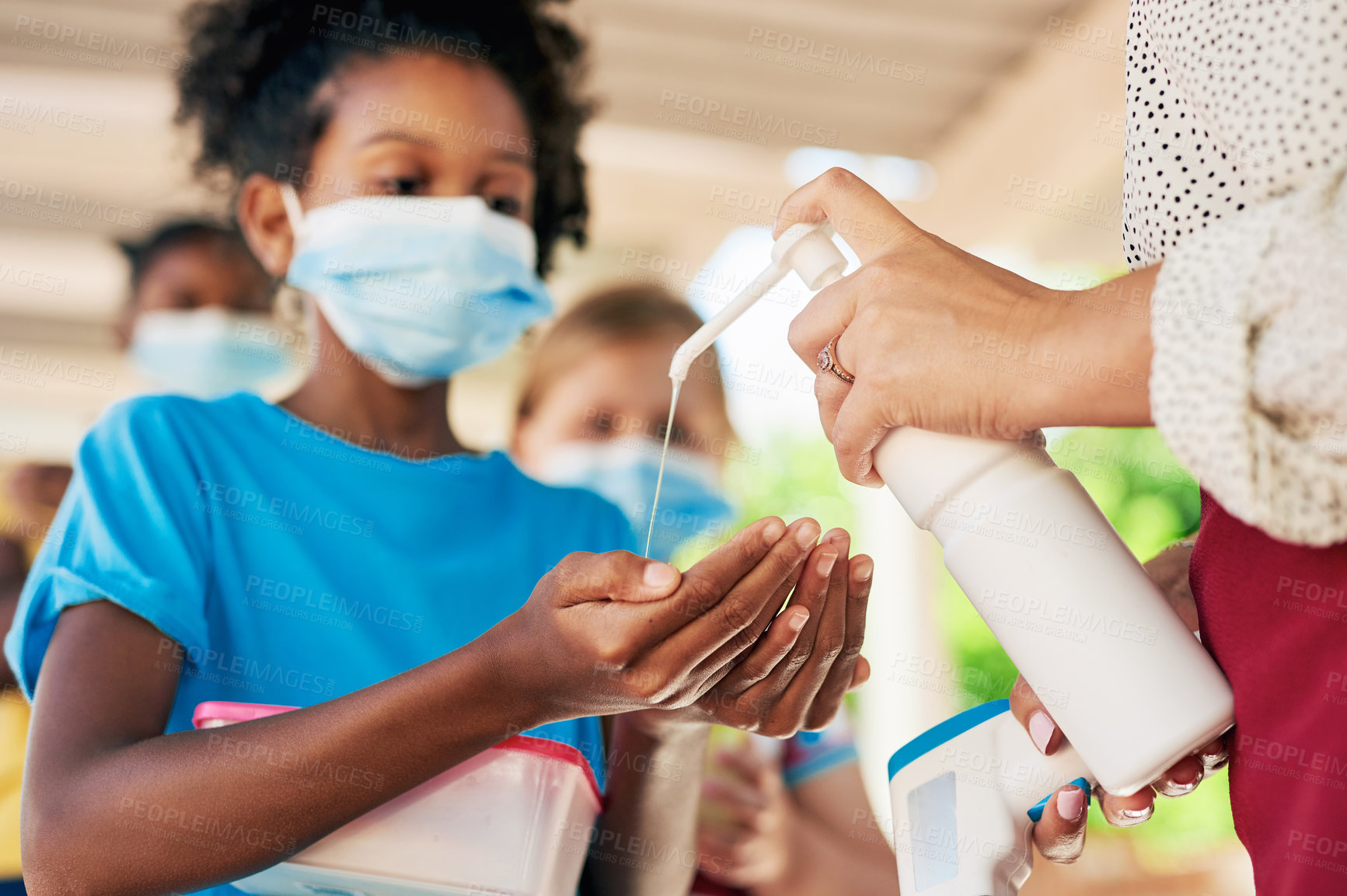 Buy stock photo Shot of a young girl wearing a face mask and sanitising her hands during recess at school