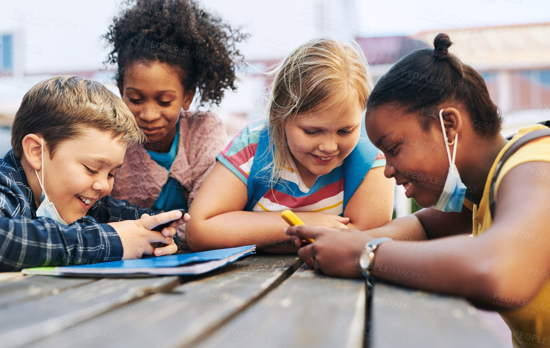 Buy stock photo Shot of a diverse group of children huddled together and using game boys to play games at school