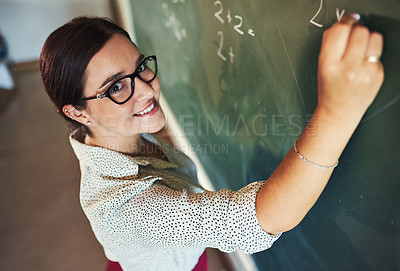 Buy stock photo Shot of an attractive young teacher standing alone and writing on the blackboard during a lesson in her classroom