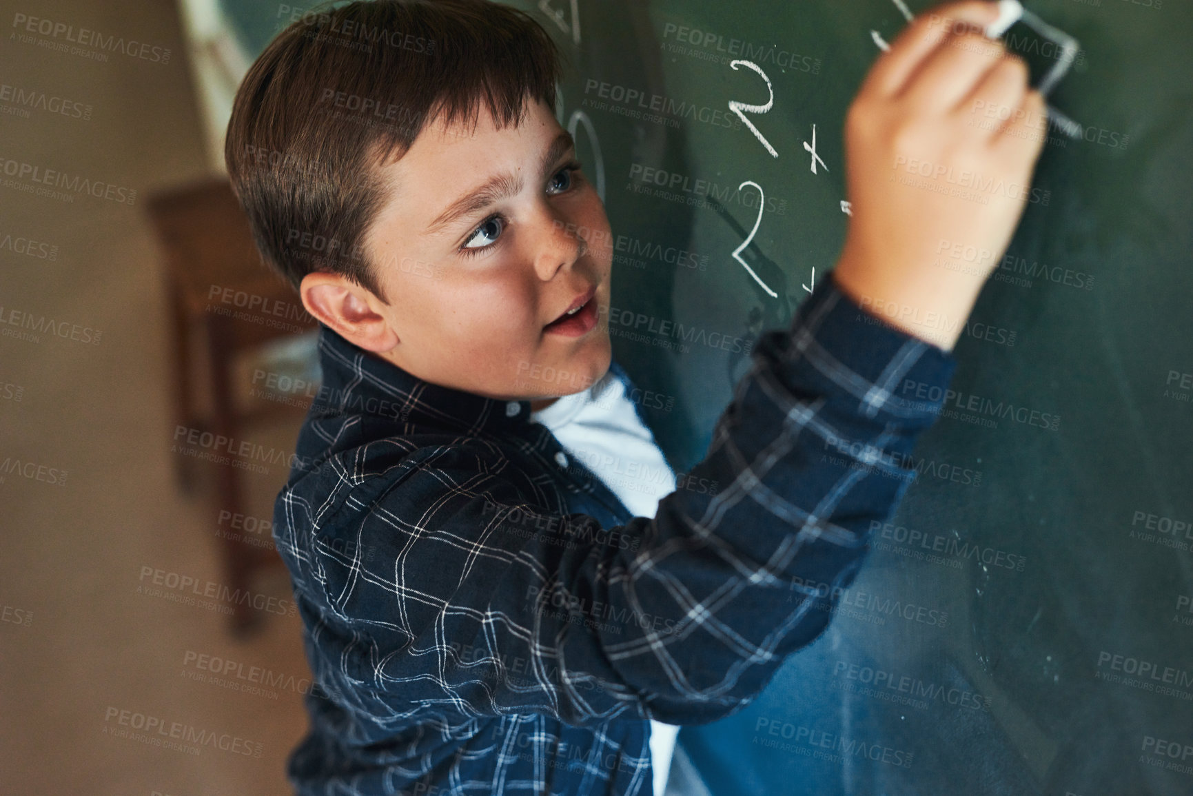 Buy stock photo Shot of a young boy standing alone and writing on the blackboard during a lesson in his classroom at school