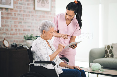 Buy stock photo Shot of a young nurse sharing information from her digital tablet with an older woman in a wheelchair