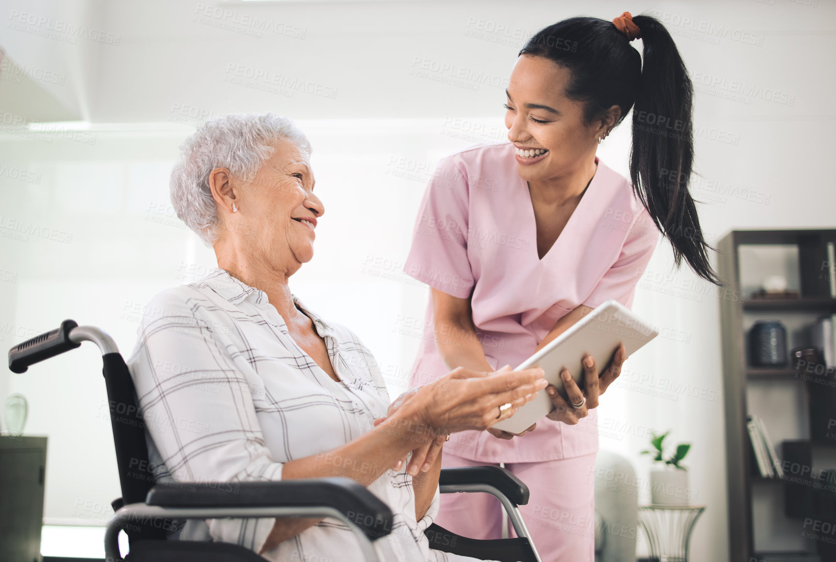 Buy stock photo Shot of a young nurse sharing information from her digital tablet with an older woman in a wheelchair