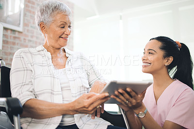 Buy stock photo Shot of a young nurse sharing information from her digital tablet with an older woman in a wheelchair