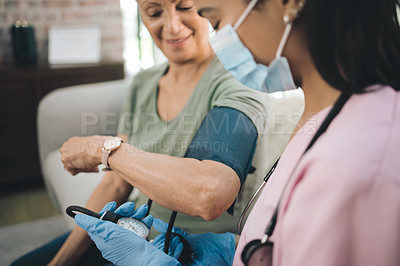 Buy stock photo Shot of a masked doctor reading her patients blood pressure at home