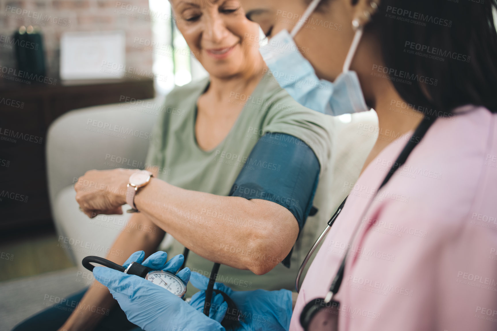 Buy stock photo Shot of a masked doctor reading her patients blood pressure at home