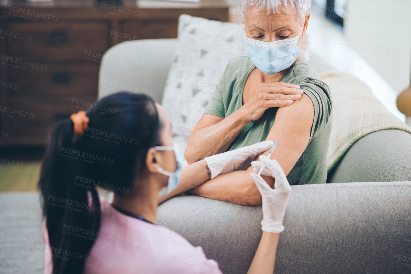 Buy stock photo Shot of a doctor giving a masked older woman an injection at home