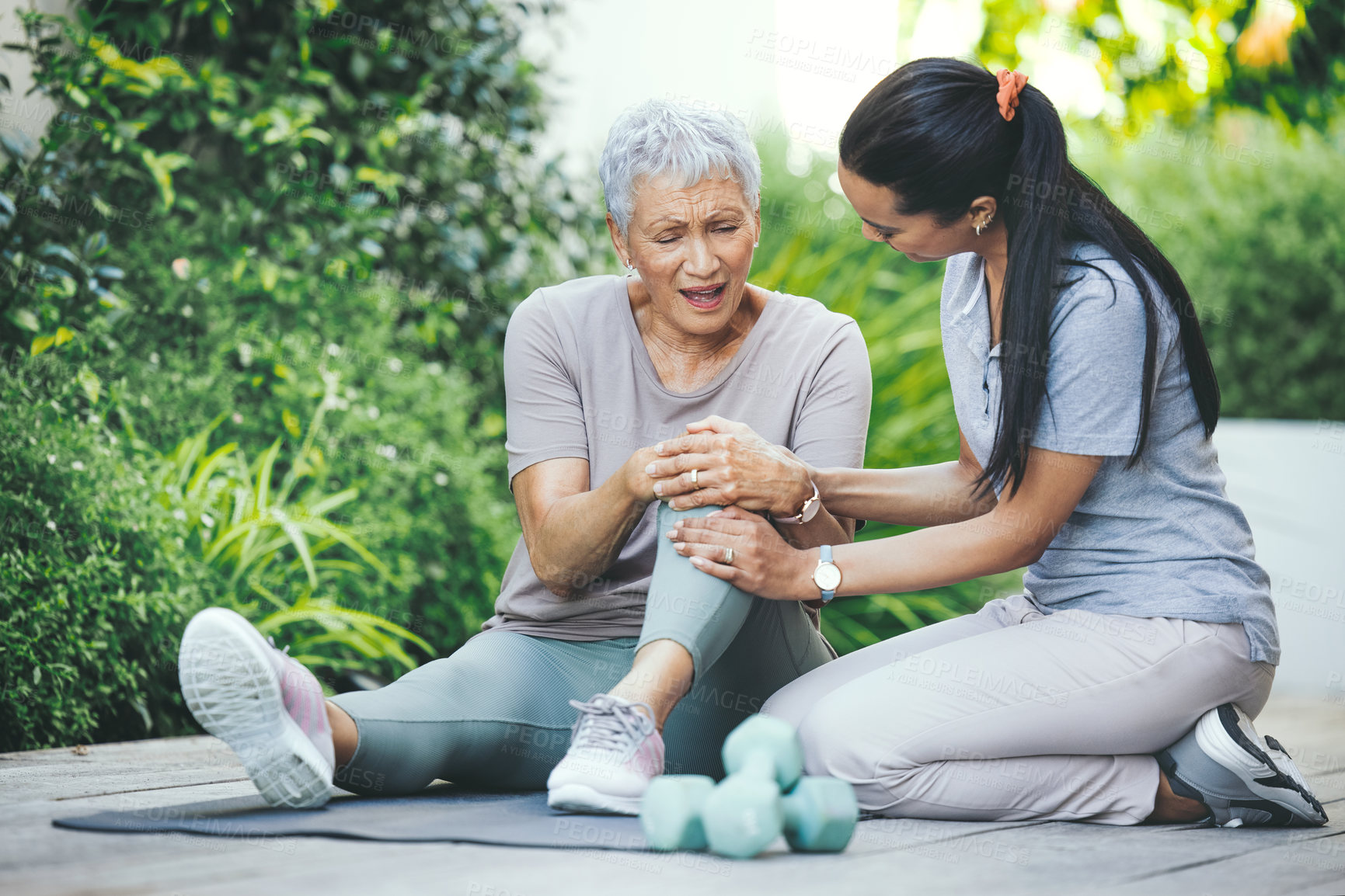 Buy stock photo Shot of an older woman holding an injured knee during a session with a physiotherapist