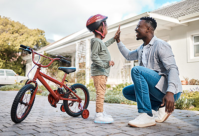 Buy stock photo Shot of a father and his son giving each other a high five while riding a bicycle outdoors