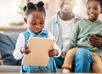 Buy stock photo Shot of an adorable little girl using a digital tablet with her family in the background at home