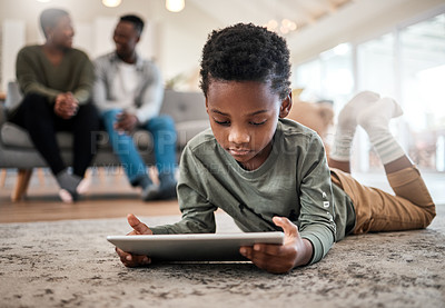 Buy stock photo Shot of an adorable little boy using a digital tablet with his family in the background at home