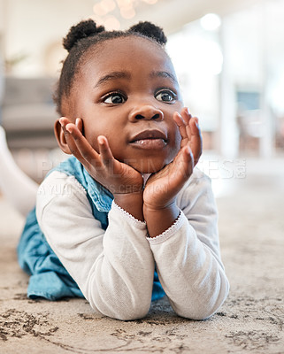Buy stock photo Shot of an adorable little girl liyng on the floor at home and looking thoughtful