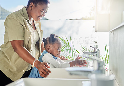 Buy stock photo Shot of a mother helping her daughter wash her hands at a tap in a bathroom at home