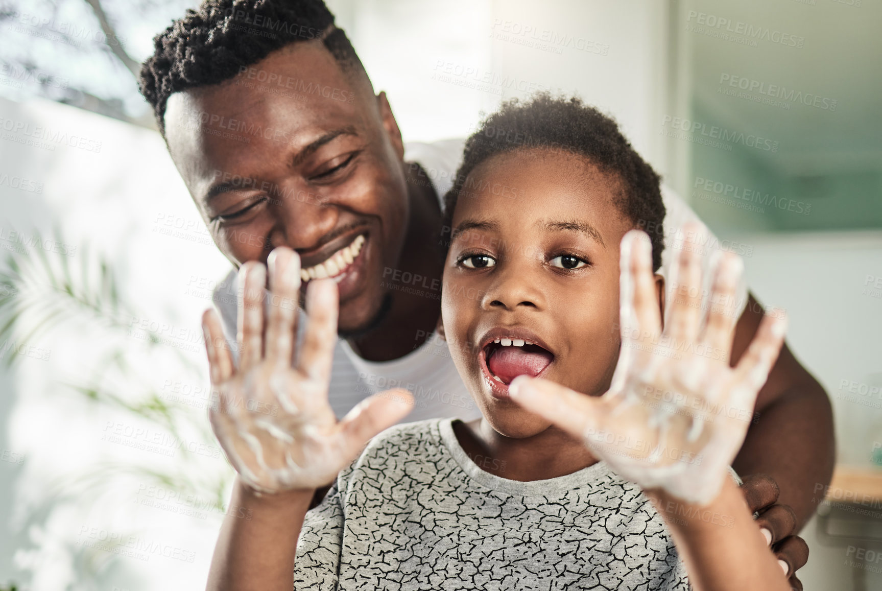 Buy stock photo Portrait of a boy holding up his soapy hands while standing in a bathroom with his father at home