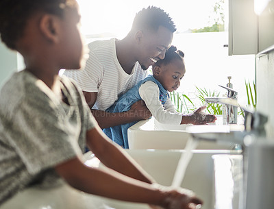 Buy stock photo Shot of a father helping his children wash their hands in a bathroom at home